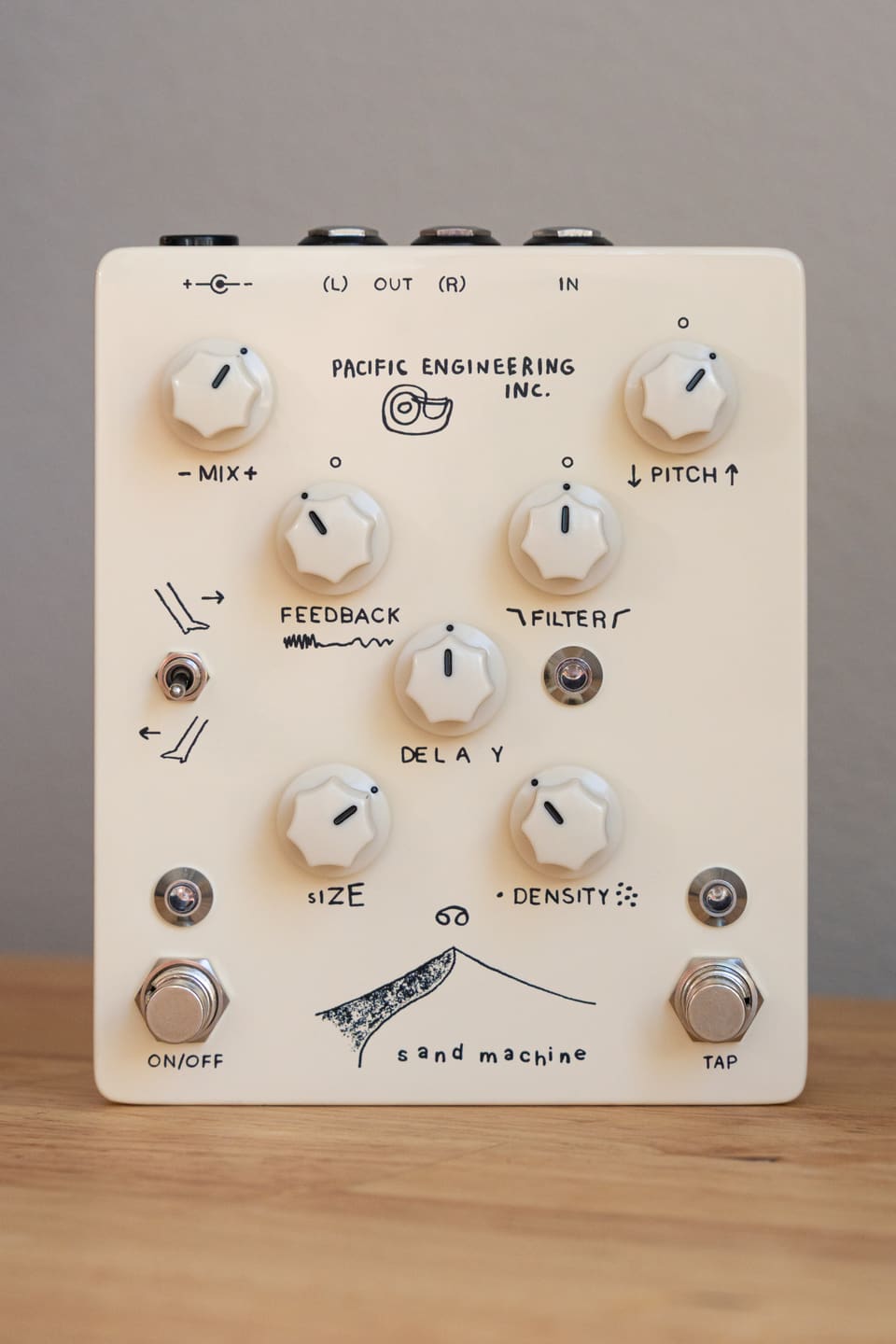 The Sand Machine — a cream granular delay pedal with hand-drawn labels — standing upright on a wooden desk